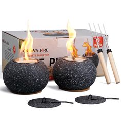 two black stone candles with flames in them next to a box of forks and tongs