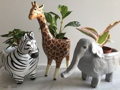 three ceramic animals are standing next to each other in front of plants and houseplants