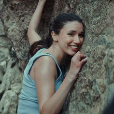 a woman is smiling and leaning against a rock