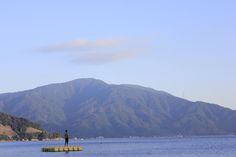 a man standing on the edge of a body of water with mountains in the background