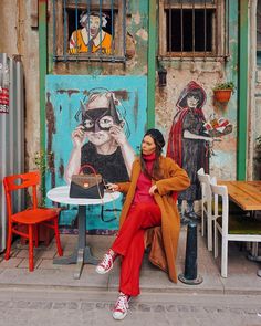 a woman sitting at a table in front of a building with graffiti on it and an orange chair next to her