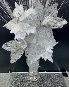 a silver vase filled with white flowers on top of a glass table covered in glitter