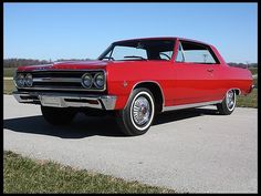 an old red car is parked on the side of the road in front of some grass