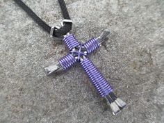 a cross made out of purple and silver wire on a black leather cord is laying on the ground