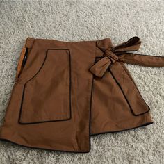 Super Cute Asymmetrical Decorative Side Tie Skirt. Never Worn. Caramel Brown With A Navy/Black Trim With Zipper On The Side Trendy High-waist Brown Skort, Brown Lined Mini Skort, Brown Asymmetrical Skirt For Fall, Casual Brown Asymmetrical Skirt, Trendy Brown Skort With Pockets, Brown Mini Skort With Pockets, Spring Brown Mini Skirt With Pockets, High Waist Brown Skort With Pockets, Brown Mini Skirt With Pockets For Spring