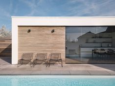 four chairs sitting on the side of a pool next to a building with sliding glass doors