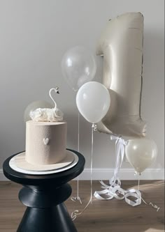 a birthday cake with balloons and streamers on a table in front of a chair