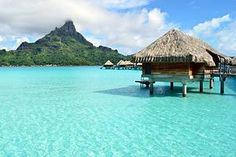 the water is crystal blue and there are huts on stilts in the middle of it