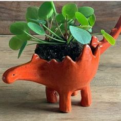 an orange dinosaur planter with green plants in it