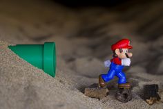 a toy mario running in the sand next to a green cone