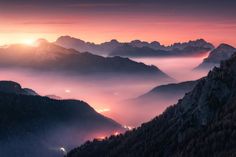 the sun is setting over mountains with fog in the valleys and low lying clouds below