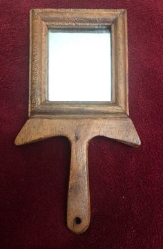 a mirror hanging on the wall with a wooden frame and an arrow shaped like a paintbrush