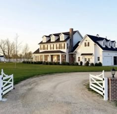 a large white house sitting on top of a lush green field next to a dirt road