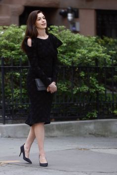 a woman in a black dress is walking down the street with her hand on her hip