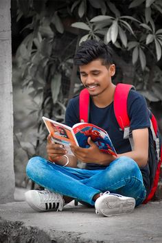 a young man sitting on the ground reading a book