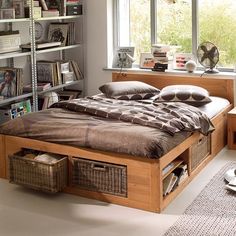 a bed sitting under a window next to a book shelf