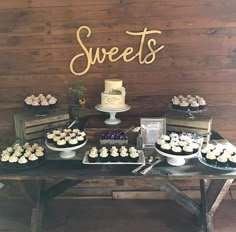 a table topped with lots of cupcakes next to a wooden sign that says sweets