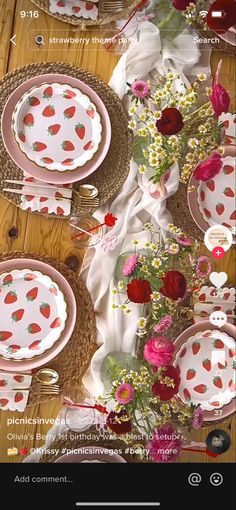 the table is set with pink and white plates, silverware, and red flowers