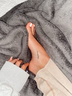 a woman's bare feet with tattoos on them laying on a gray and white blanket