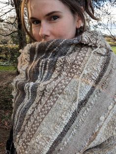 a woman wrapped in a blanket standing next to a tree and looking at the camera