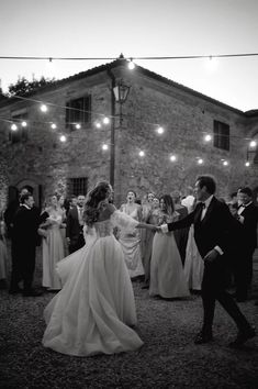 the bride and groom are dancing in front of their wedding party at night with string lights