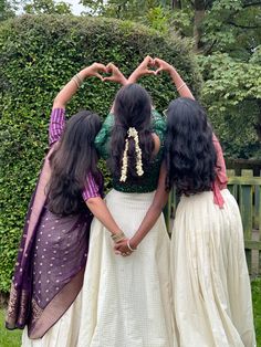 three women standing in front of a hedge making the shape of a heart with their hands