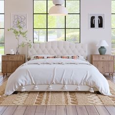 a white bed sitting in a bedroom on top of a wooden floor next to two windows