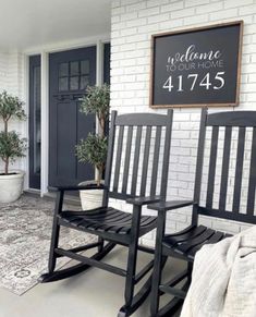 two black rocking chairs sitting in front of a white brick wall with a welcome sign above them