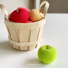 two crocheted apples in a basket next to an apple on a white table