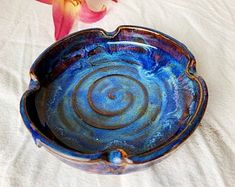 a blue bowl sitting on top of a white bed next to a pink and yellow flower