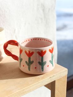 a cup sitting on top of a wooden table next to a vase with flowers painted on it