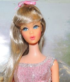 a close up of a doll with blonde hair and blue eyes wearing a pink dress