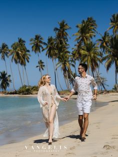 a man and woman walking on the beach holding hands with palm trees in the background