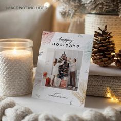 a holiday card sitting on top of a table next to some pine cones and candles