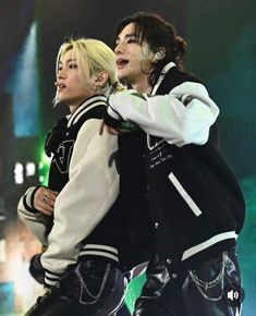 two people standing next to each other with their arms around one another while wearing black and white jackets