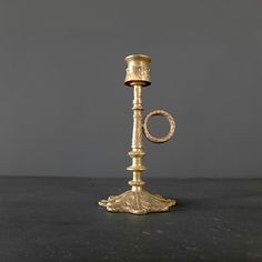 an antique brass candle holder on a black table with a gray wall in the background