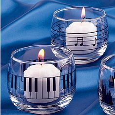 three candles with music notes on them are sitting in glass bowls and one candle is lit