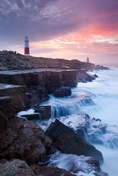 a lighthouse on top of a cliff next to the ocean with waves crashing against it