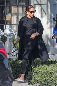 a woman in black coat and pants walking down the street