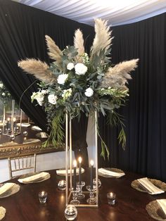 a tall vase filled with flowers and greenery on top of a dining room table