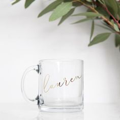 a glass mug with the word lauren written on it next to a potted plant