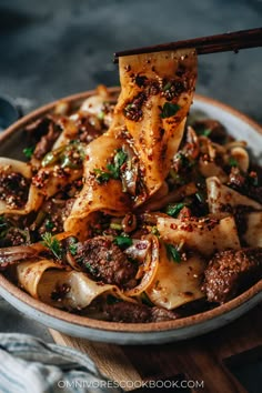 a bowl filled with pasta and meat on top of a wooden cutting board next to chopsticks