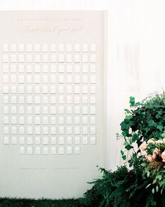 a white calendar sitting on top of a table next to flowers and greenery in front of a wall