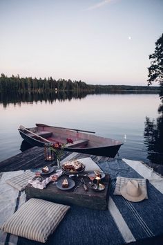 a table with food on it next to a boat in the water and some trees