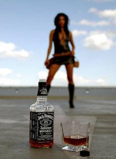 a woman standing next to a bottle of whiskey and a shot glass on the ground