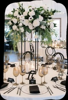 a table set with white flowers and wine glasses on it for a formal dinner or party