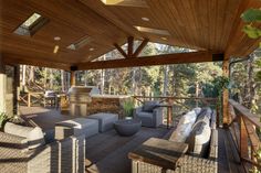 a covered patio with furniture and an outdoor grill area in the background, surrounded by pine trees