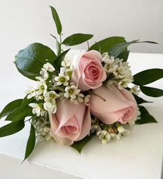 a bouquet of pink roses and white flowers on top of a table with green leaves