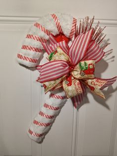 a candy cane wreath hanging on the front door with christmas decorations and ribbons attached to it