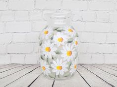 a glass vase with daisies painted on it